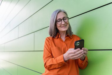 Gülümseyen son sınıf öğrencisi elinde akıllı telefonla gezici uygulama alışverişi yapıyor. Sokakta duruyor. 