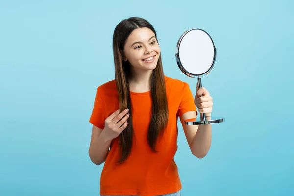 Pretty teenege girl looking in mirror isolated on blue background. Skin care morning routine concept