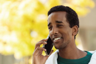 Yakın plan portresi, gülümseyen Afro-Amerikan bir adamın cep telefonu tutarken, konuşurken, başka tarafa bakarken, kopya çekerken. Yakışıklı, genç bir iş adamı. İş konsepti, reklam