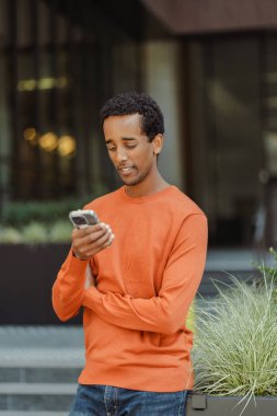 Çekici gülümseyen Afrikalı Amerikalı adamın portresi cep telefonu mesajı okuyor, internette iletişim kuruyor. 