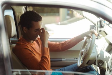 Üzgün, yorgun Afrikalı Amerikalı erkek sürücü direksiyonda oturuyor trafikte, acele içinde. Ulaşım kavramı