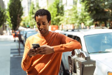 Yakışıklı Afro-Amerikan bir adamın portresi şık günlük kıyafetler giyen, cep telefonu iletişimini çevrim içi tutan, açık ekrana bakan. Çekici genç öğrenci arabanın yanında duruyor. 