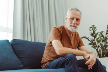 Oturma odasındaki yumuşak koltukta oturan ve yüzünü çeviren yakışıklı, yaşlı bir adam. Kahverengi tişört giyen kendinden emin büyükbaba, başka tarafa bakıyor. Reklam kavramı