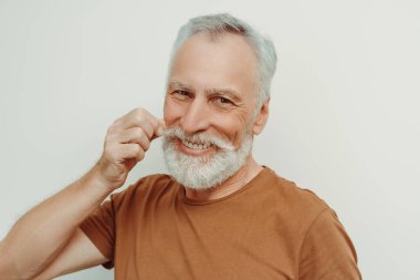 Çekici gülümseyen, sakallı, bıyıklı yaşlı adam, gri arka planda izole edilmiş kameraya bakıyor. Kahverengi tişörtlü, şık saçlı, resim için poz veren yakışıklı bir erkek. Reklam kavramı