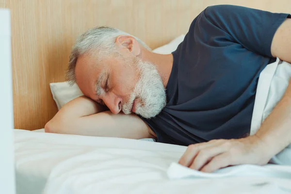 Closeup portrait of attractive senior man lying on bed with closed eyes covered with blanket sleeping resting in living room. Handsome elderly male posing for picture. Advertisement concept