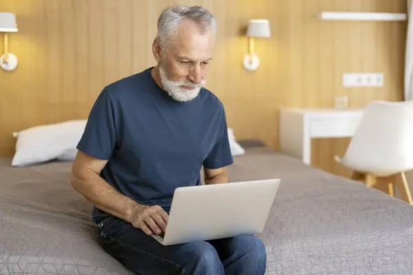 老年人坐在客厅的床上 使用笔记本电脑 打字机打字 远程工作的肖像 专业的高级程序员在家里工作 技术概念 — 图库照片
