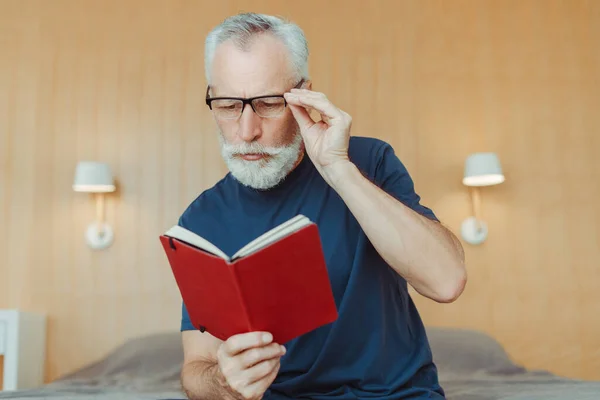 多愁善感的老年人头戴眼镜 拿着笔记本 坐在客厅的床上的画像 身穿休闲装的老年养恤金领取者 正在学习 教育概念 — 图库照片