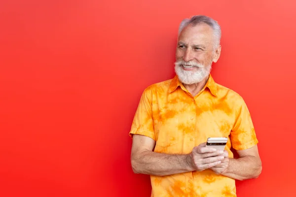 英俊的老人微笑着把手机放在网上购物 隔离在红色背景的街道上 复制空间 多愁善感的大胡子嬉皮士使用智能手机 在线交流 移动银行 — 图库照片