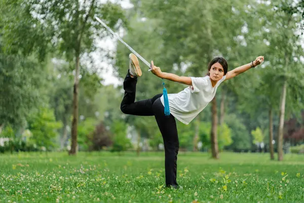Martial arts woman practicing wushu kungfu with sword at green park. Healthy wellness active training concept