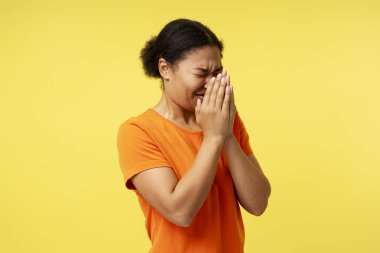 Virüs salgını, grip salgını. Hasta Afro-Amerikalı kadın elleriyle hapşırıyor, burnu temizliyor, öksürüyor, grip belirtileri gösteriyor, ateşi var. Sarı arka planda kapalı stüdyo çekimleri 