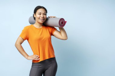 Elinde yoga minderiyle gülümseyen Afrikalı Amerikalı bir kadının portresi. Eğitimleri mavi arka planda gözlerden uzak. Spor, sağlıklı yaşam tarzı konsepti