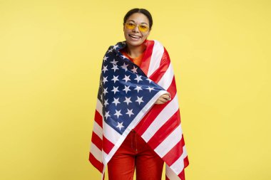 Sarı arka planda Amerikan bayrağı taşıyan, kendinden emin gülümseyen Afro-Amerikan kadın portresi Bağımsızlık Günü 'nü kutluyor. 4 Temmuz konsepti 