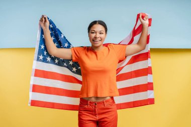 Kendinden emin gülümseyen Afro-Amerikan kadının Amerikan bayrağını tutan portresi Ukrayna bayrağında izole edilmiş. Destek konsepti 