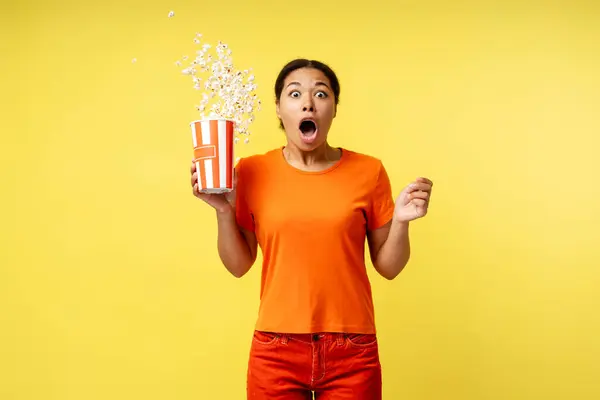 若い興奮したアフリカ系アメリカ人女性がポップコーンでバケツを持って 黄色の背景に隔離された口で映画を見ているスナックを食べます シネマタイム 広告コンセプト — ストック写真
