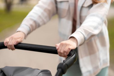 Yakından, bebek arabasını iten genç bir kadın, seçici odaklanma. Bebekle dışarıda yürümek.