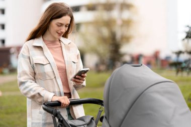 Gülümseyen genç anne cep telefonu kullanıyor, yeni doğmuş bebeğiyle bebek arabasında yürüyor. Parkta çocuklu güzel bir kadın, mektupları kontrol ediyor, online alışveriş yapıyor.