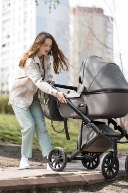 Canı sıkkın genç bir anne bozuk asfalt üzerinde yürüyor, engeller ve yeni doğmuş bebekle bebek arabasını itiyor. Parkta çekici bir kadın.