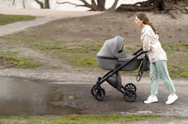 Yürümekten memnun olmayan genç bir anne, büyük su birikintisi ve yeni doğmuş bebekle bebek arabasını itmek. Parkta çekici bir kadın.