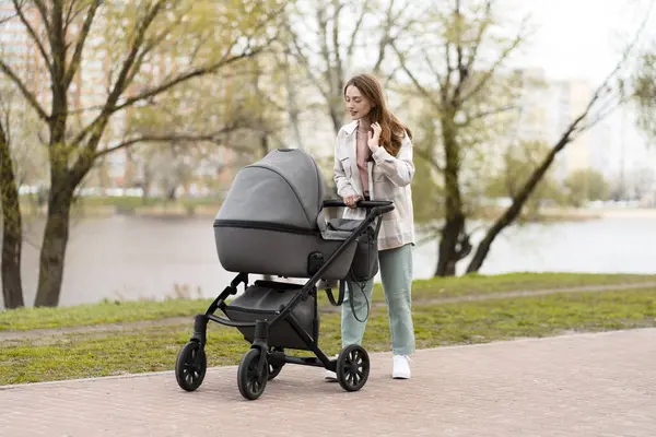 Positieve Jonge Vrouw Duwen Kinderwagen Met Baby Het Park Stad — Stockfoto