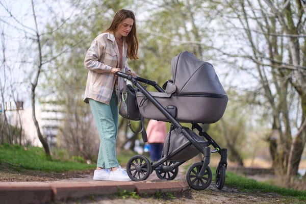 在城市公园散步时 白人年轻母亲艰难地推着婴儿车从路边俯冲而下的全影 — 图库照片