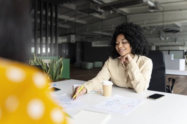 Kendine güvenen Afrikalı kadın, ofis çalışanı meslektaşları veya iş ortaklarıyla grafikler ve diyagramlar tartışıyor, modern şirket binasının iç kısımlarında masa başında oturuyor. Satış departmanı. - İnsanlar. Kariyer