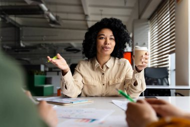 Amaçlı Afrikalı Amerikalı kadın yönetici, hazır kahve bardağını tek kullanımlık kağıt bardakta tutuyor, iş planlarını tartışıyor, fikirleri paylaşıyor, toplantı odasında konferans düzenlerken yeni bir proje planlıyor.