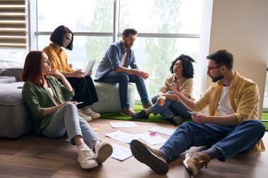 Yaratıcı tasarımcılar, serbest girişimciler, iş ortakları ve meslektaşlar yeni bir proje üzerinde çalışırken, rahat bir dostane atmosferde dizüstü bilgisayar ve grafikler ve şemalar kullanıyorlar.