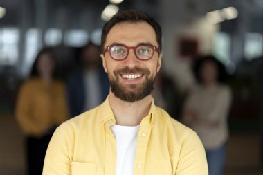 Sıradan giyinmiş, modaya uygun gözlük takan, şirket ofisinde kameraya güvenle gülümseyen beyaz, yakışıklı bir adamın kendine güvenen portresi. - İnsanlar. Şirket işi. Meslek