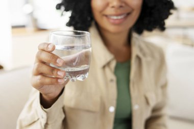 Elinde bir bardak suyla gülümseyen güzel Afro-Amerikan kadının portresi, elinde seçici bir odaklanma. * Sağlık hizmetleri dışında, ferahlatıcı *