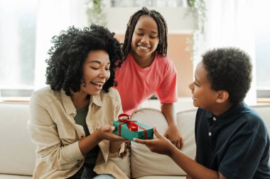 Doğum gününde güzel annelerine evde otururken hediye veren gülümseyen Afro-Amerikan çocukların portresi. İlişki kavramı, annelik.
