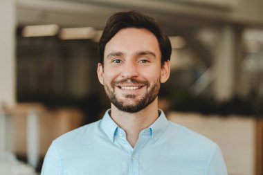 Yakışıklı, gülümseyen İspanyol işadamının portresi, modern ofiste çalışan. Kendine güvenen sakallı satıcı kameraya bakıyor. Başarılı iş konsepti