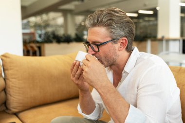 Pozitif gri saçlı iş adamının portresi rahat koltukta oturuyor gözleri kapalı kahve içiyor modern ofiste kahve molası veriyor.