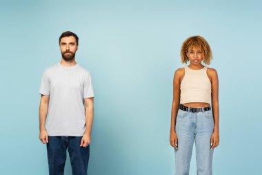 Mavi arka planda izole edilmiş kameraya bakan çok ırklı beyaz erkek ve Afro-Amerikan kadın portresi.
