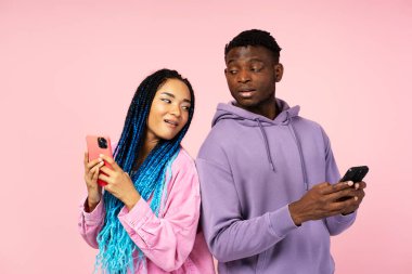 Güzel Afro-Amerikalı kadın ve şık giyinmiş bir adamın portresi cep telefonu kullanıyor, internetten pembe arka planda izole edilmiş mesajlar alıyor. Teknoloji konsepti