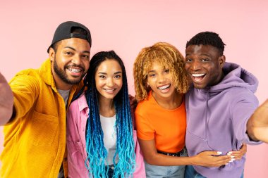 Bir grup gülümseyen arkadaş şık renkli kıyafetler giyip selfie çekiyor, sarılıyor ve pembe arka planda tek başına dikiliyorlar. Olumlu yaşam tarzı, arkadaşlık kavramı