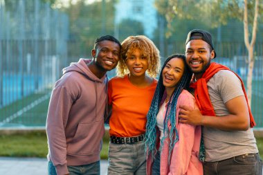 Bir grup gülümseyen stil sahibi Afrikalı Amerikalı arkadaş günlük kıyafetler giyip, kucaklaşıp, sokakta yan yana duran kameralara bakıyorlar. Olumlu yaşam tarzı, arkadaşlık kavramı 