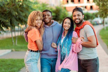 Bir grup gülümseyen Afro-Amerikan öğrenci kucaklaşıyorlar, dışarıda duruyorlar, üniversite kampüsünün yakınında, kameraya bakıyorlar. Arkadaşlık kavramı