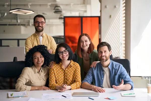 Business people in the meeting room, planning business strategy or brainstorming at the office. Confident portrait of a diverse millennial business partners sitting at desk, smiling, looking at camera