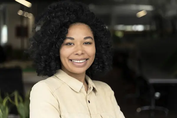 Confident portrait of a successful African American young woman, purposeful sales manager, CEO, executive director, office worker smiling looking confidently at camera, standing in corporate office