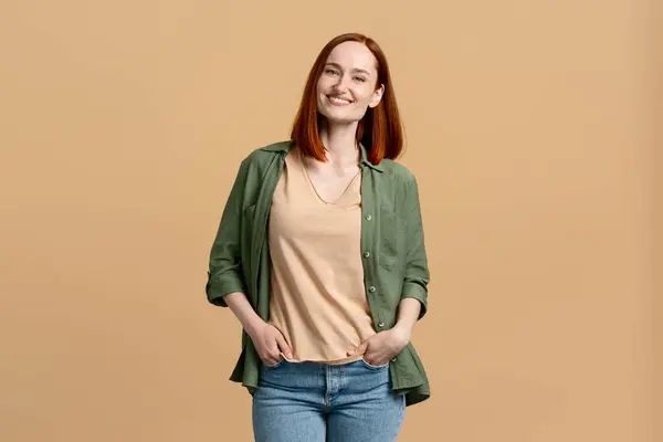 Confident studio portrait of a beautiful young ginger woman in stylish casual clothes, smiling cutely looking at camera, isolated on beige background. People. Emotions. Lifestyles. Professions