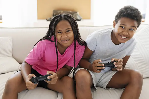 英俊而积极的非洲裔美国人姐姐和兄弟拿着操纵杆在客厅沙发上玩电子游戏的肖像 积极的孩子在网上玩得很开心 童年概念 — 图库照片