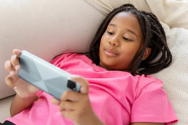 美しく 興奮するアフリカ系アメリカ人の少女は 携帯電話を持って横たわり ゲームをしたり ソーシャルメディアをしたり リビングルームで自宅で過ごしたりしている ブラウジングコンセプト — ストック写真