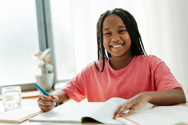 美しい笑顔のアフリカ系アメリカ人女子高生の肖像画が教室の机に座り ペンを抱き メモを取って カメラを見て試験の準備をしている 教育コンセプト — ストック写真