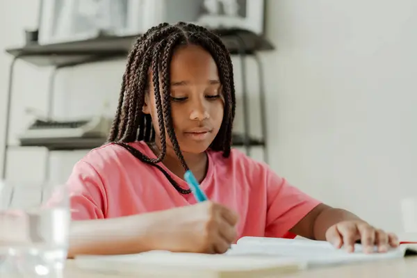 スマートなアフリカ系アメリカ人の少女の肖像画 教室に座り テーブルに座り 宿題をし ペンを握り 書き留めた 学校のコンセプトに戻る — ストック写真