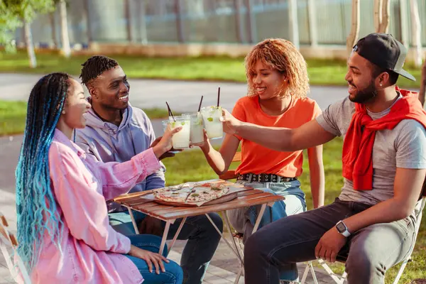 Group of diverse smiling African American friends, meeting at birthday party, sitting in cafe, clinking lemonades outdoors. Celebration concept