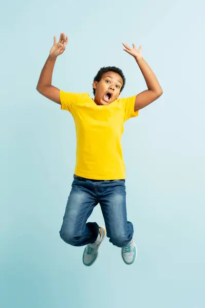 穿着休闲装的兴奋的非洲男孩的画像 手举起来跳跃 被蓝色背景隔离 可爱的孩子在镜头前玩得很开心 童年概念 — 图库照片