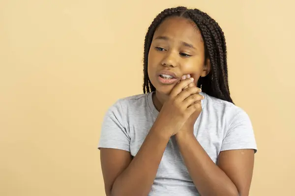 令人心烦意乱的美丽的非洲裔美国女孩 留着时髦的辫子 摸着脸颊 在米色的背景上孤立无援 可悲的女孩 牙科护理概念 — 图库照片