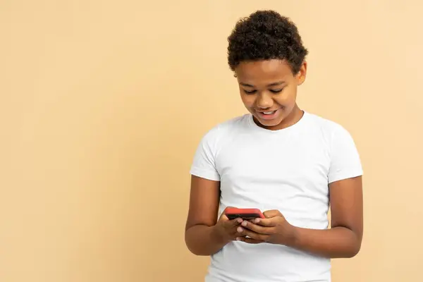 笑顔のハンサムなアフリカ系アメリカ人の少年 携帯電話 テキストメッセージ ベージュの背景で隔離されたオンラインショッピング コピースペース ソーシャルメディアコンセプト — ストック写真