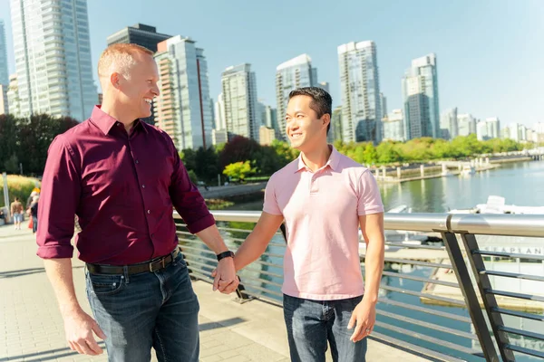 Portrait of smiling two homosexual men, gay couple holding hands looking at each other walking on urban street, travel. Date, relationship, love concept