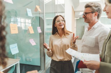 Gülümseyen iş kadını gözlük takıyor yapışkan notlar kullanıyor, üretkenlik için çevik metodoloji modern ofiste birlikte çalışıyor. Scrum ana planlama stratejisi, iş arkadaşlarıyla konuşmak.